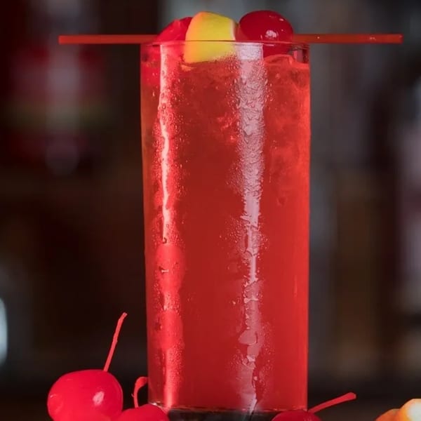 A tall glass of red Jamaican drink, garnished with cherries and a lemon slice.
