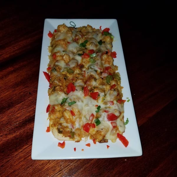 Duckanoo Grill's cheesy Jamaican flatbread topped with chicken, red peppers, and green onions.