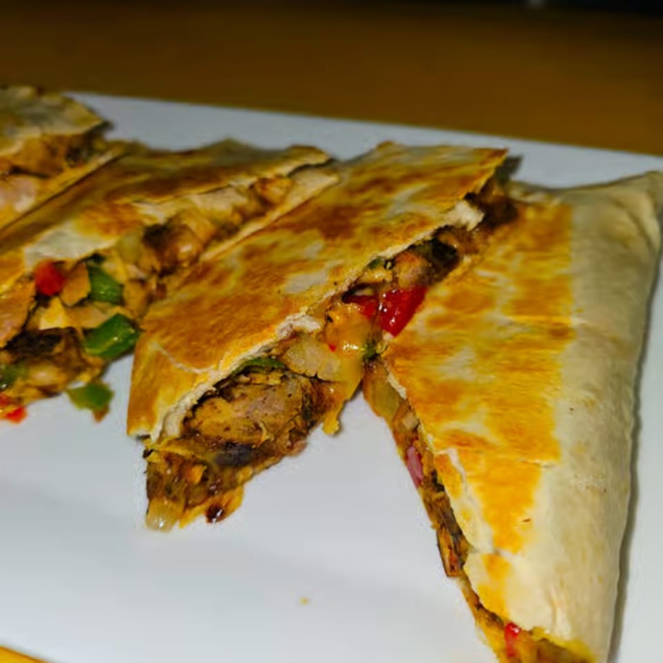 Close-up of Jamaican jerk chicken quesadillas with red and green peppers, onions, and melted cheese.