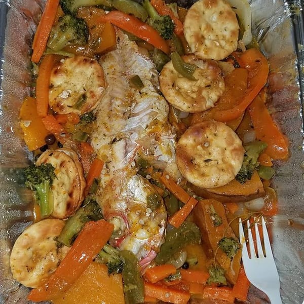 Steamed fish with carrots, broccoli, peppers, and crackers in a foil container.