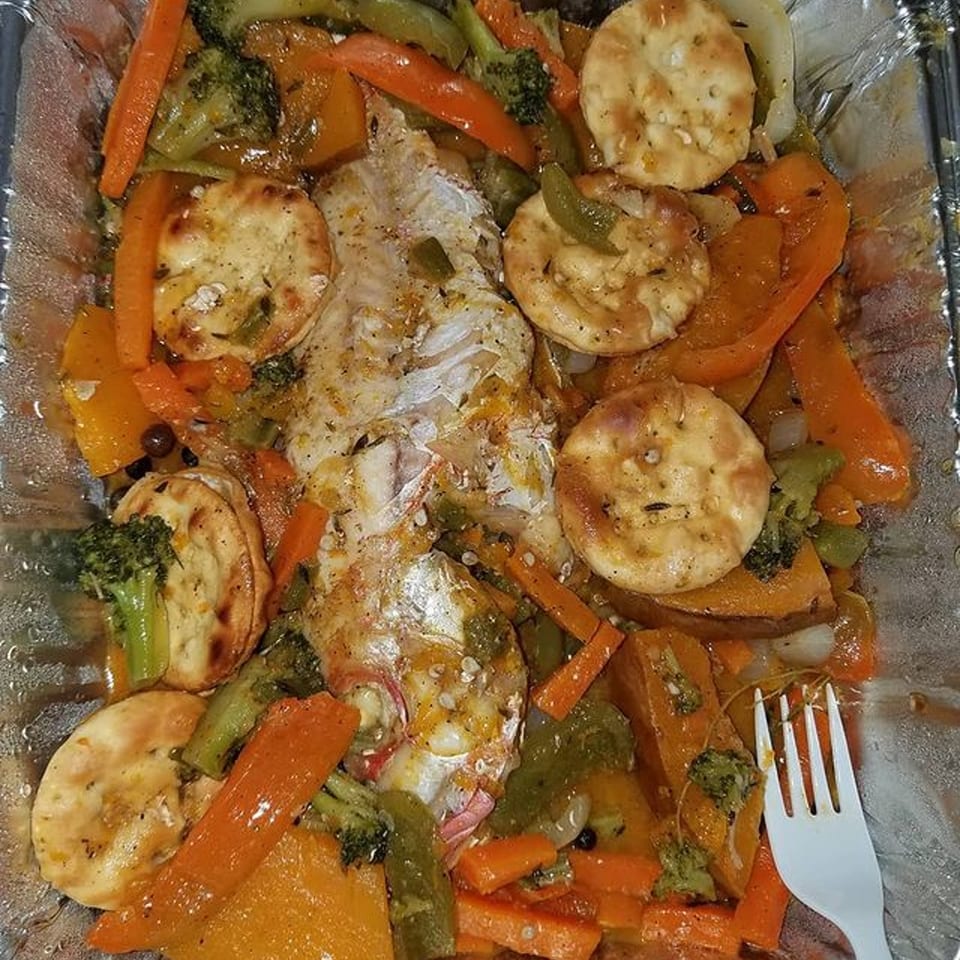 Steamed fish with carrots, broccoli, peppers, and crackers in a foil container.