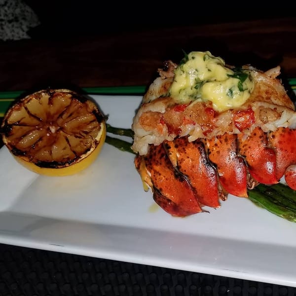 Grilled lobster tail with herb butter, asparagus, and a charred lemon half on a white plate.